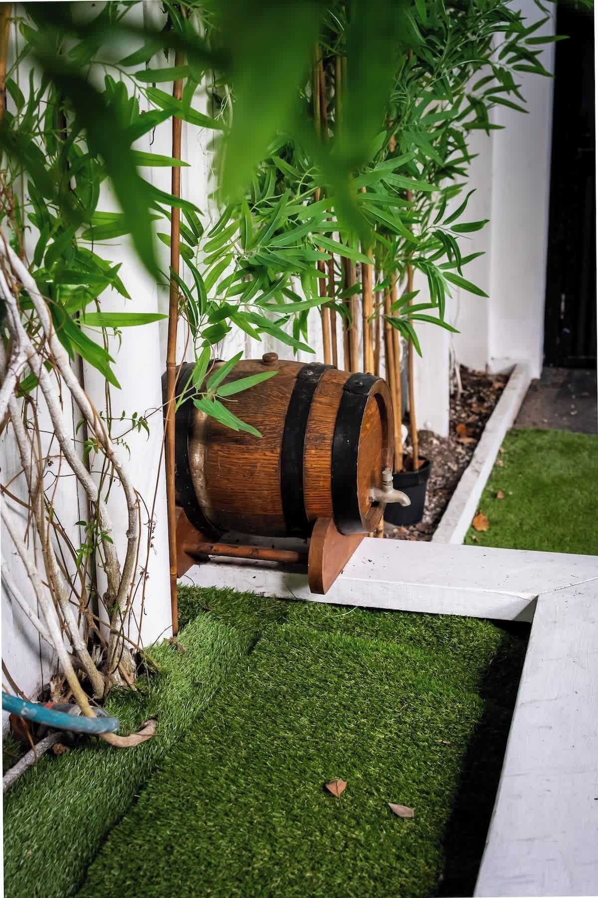 Ein Fass in einem Garten mit Kunstgrashalm und Bambuspflanzen.