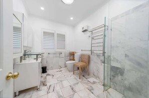 Ein Badezimmer mit Duschkabine aus Glas, einem weißen Waschbecken, einer Toilette und einem Stuhl.