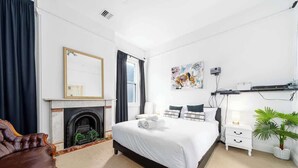 A bedroom with a bed, a fireplace, a mirror, a nightstand, a lamp, and a plant.