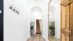 A hallway with a wooden floor, white walls, a staircase, and a large mirror with ornate gold detailing.
