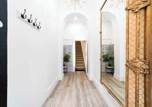 Ein Korridor mit Holzboden, weißen Wänden, einer Treppe und einem großen Spiegel mit aufwendiger Goldverzierung.