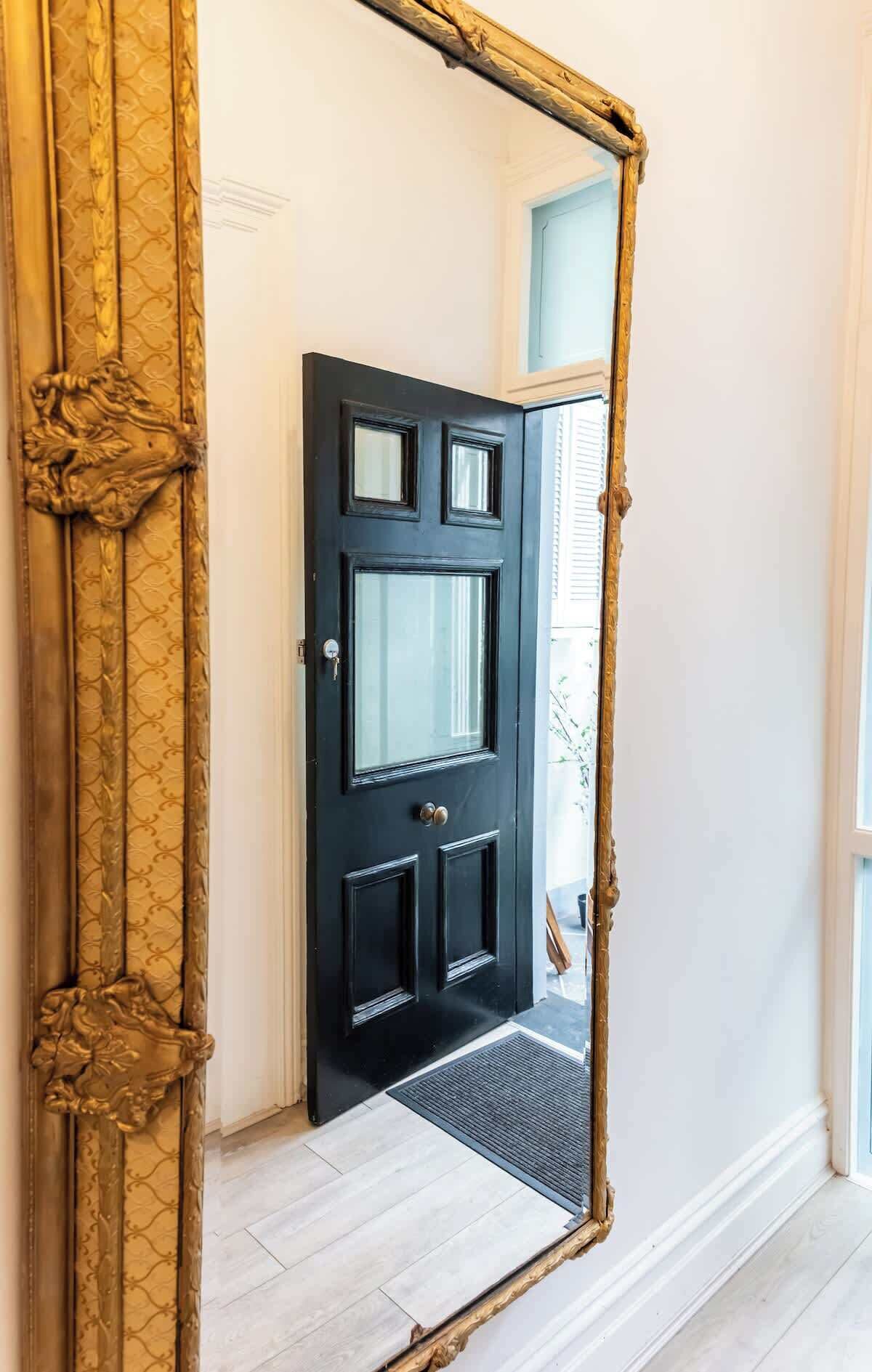 A black door with a keyhole and a doorknob, flanked by a golden ornate mirror frame.