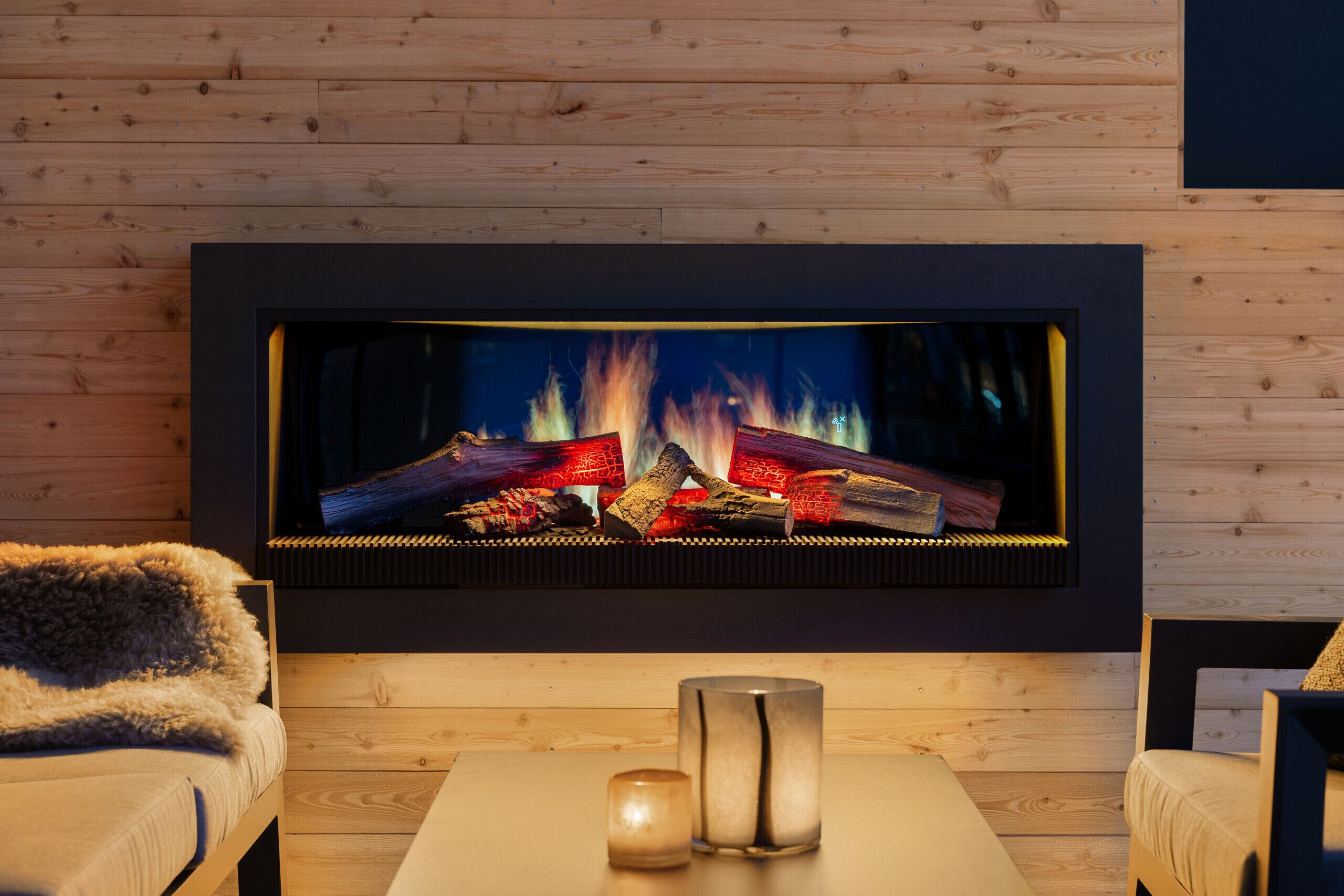 Een moderne haard met houten bovenkant, een bank en een tafel met kaarsen.