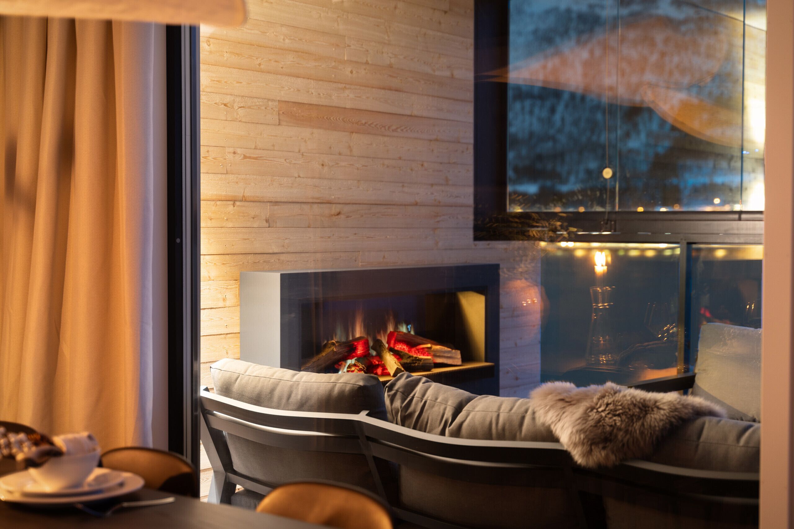 A modern living room with a fireplace, a sofa with a fur throw, and a dining area with a table and chairs.