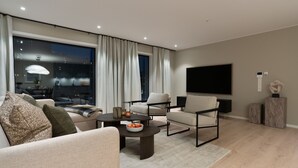 Een moderne woonkamer met een bank, fauteuils, een salontafel en een flatscreen televisie.