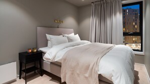 Een moderne slaapkamer met een bed, nachtkastje en een raam met gordijnen.
