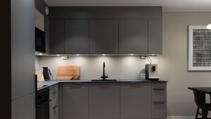 Een moderne keuken met grijze kastjes, een houten snijplank, een koffiezetapparaat en een wandairconditioner.