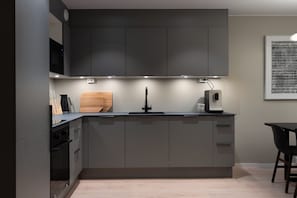 A modern kitchen with grey cabinets, a wooden cutting board, a coffee maker, and a wall-mounted air conditioner. - Premium Waterfront Apartment with Stunning View (Tromsø)