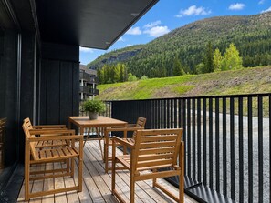 Een houten terras met een tafel en stoelen, met uitzicht op een bergachtig landschap.