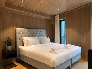 Een groot bed met een gestuufd hoofdeinde, wit beddengoed en opgerolde handdoeken op het bed.