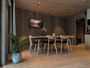 Een eetgedeelte met een houten tafel en stoelen, een potplant en een schilderij aan de muur.