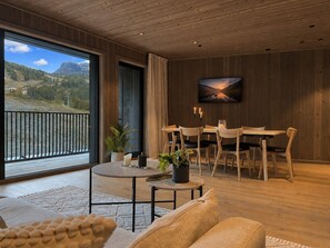 Un interior modern amb una zona de menjador, un finestral gran amb vista a la muntanya i un quadre a la paret.