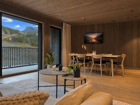 A modern interior with a dining area, a large window with a mountain view, and a painting on the wall.