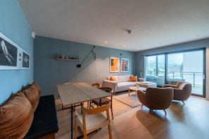 Ein modernes Wohnzimmer mit Sofa, Esstisch, Couchtisch und einem Balkon mit Aussicht.