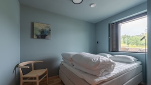 Une chambre à coucher avec un lit, une chaise, un tableau et une fenêtre donnant sur un paysage.