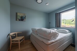 Ein Schlafzimmer mit Bett, Stuhl, einem Gemälde und einem Fenster mit Blick.