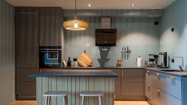 Une cuisine moderne dotée d’un îlot central, de tabourets de bar, d’un luminaire suspendu et d’un four encastré.