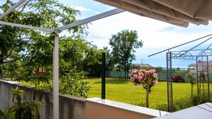 A covered outdoor area with a view of a garden, a metal structure, and a building in the background. - House Of Good Vibrations Indy (Vodnjan)
