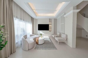 A modern living room with a flat-screen TV, a sofa, a coffee table, and a staircase. - Mabat Jasmin Greek Villa 4BR 583 Villa11 (Jeddah)