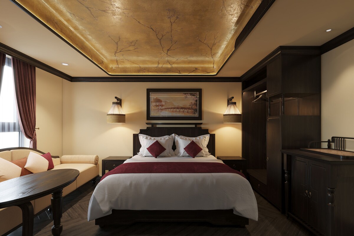 A hotel room with a large bed, bedside lamps, a wooden nightstand, a desk, and a wardrobe.