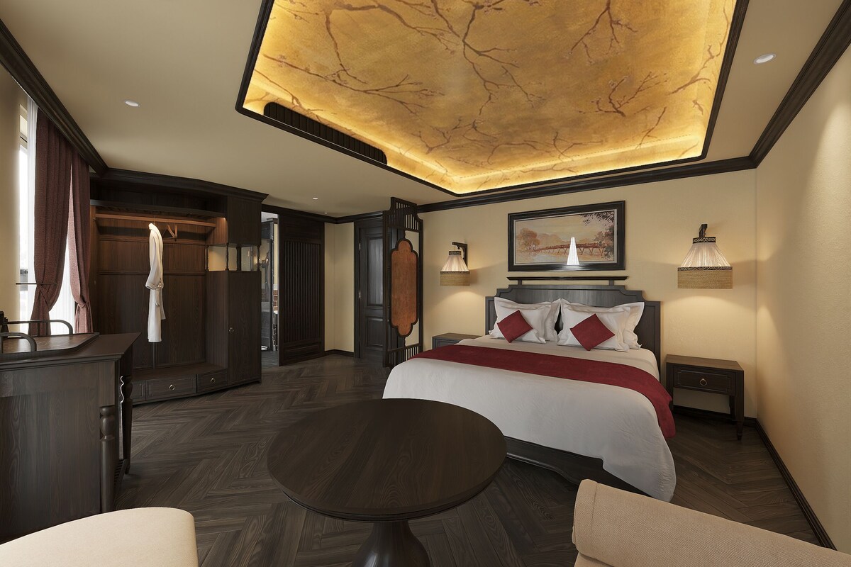 Ett hotellrum med en säng, sängbord, ett skrivbord, en stol, ett runt bord och ett tak med en unik design.