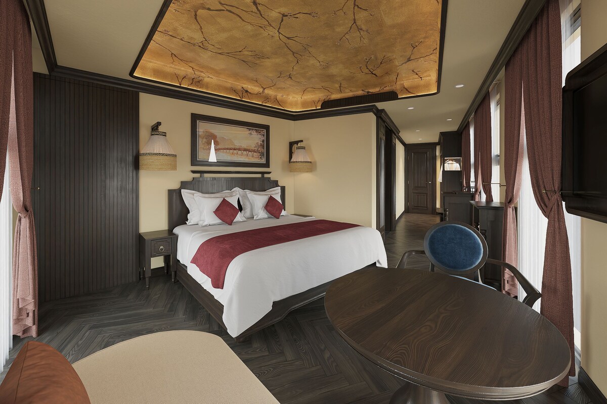 Ein Hotelzimmer mit Bett, Nachttischen, einem runden Holztisch und Blick auf den Korridor.