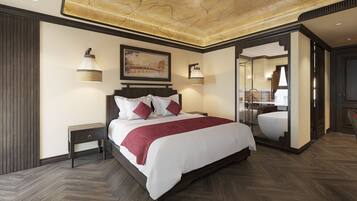 Habitación de hotel con una cama grande, suelo de madera, techo con acabado tipo mármol y baño visible a través de una puerta de cristal.