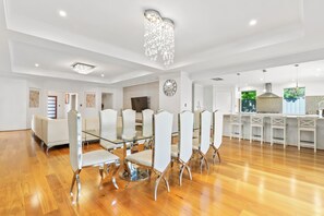 A spacious dining area with a glass table and white chairs, a kitchen with white cabinets, and a large chandelier. - Modern and luxury private Home (Piara Waters)