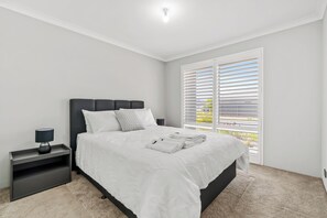 A bedroom with a bed, nightstand, lamp, and a window with blinds. - Modern and luxury private Home (Piara Waters)