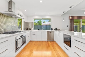 A modern kitchen with white cabinetry, a stainless steel range hood, and a large window. - Modern and luxury private Home (Piara Waters)