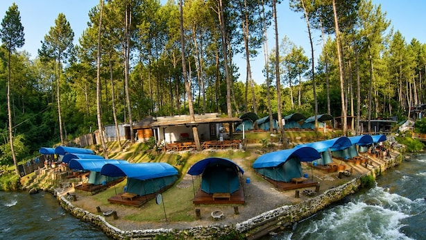 Zona de camping junto al río con tiendas de campaña y una balsa.