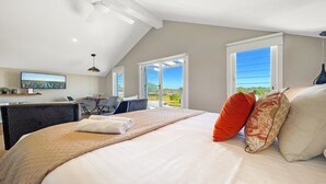Een slaapkamer met een groot bed, een bureau en een stoel, een televisie, en een balkon met uitzicht.