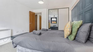 A modern bedroom with a large bed, a wardrobe, and a visible bathroom. - Modern 1-Bed Flat in Jewellery Quarter (West Midlands)