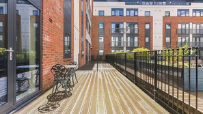 A modern building with a brick facade, large windows, and a wooden deck with outdoor furniture. - Modern 1-Bed Flat in Jewellery Quarter (West Midlands)