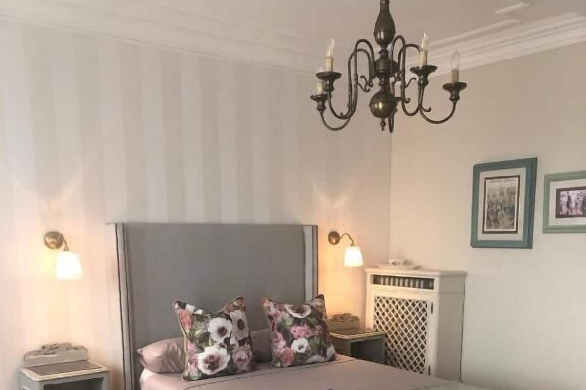 Un dormitorio con cama, mesitas de noche, una araña y l ámparas de pared.