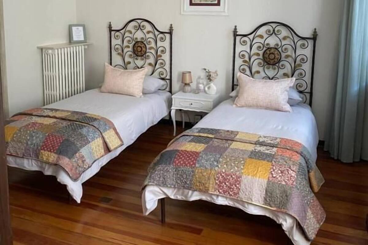 Un dormitorio con dos camas, una mesita de noche con lámpara, un cuadro enmarcado en la pared y un cabecero de madera.
