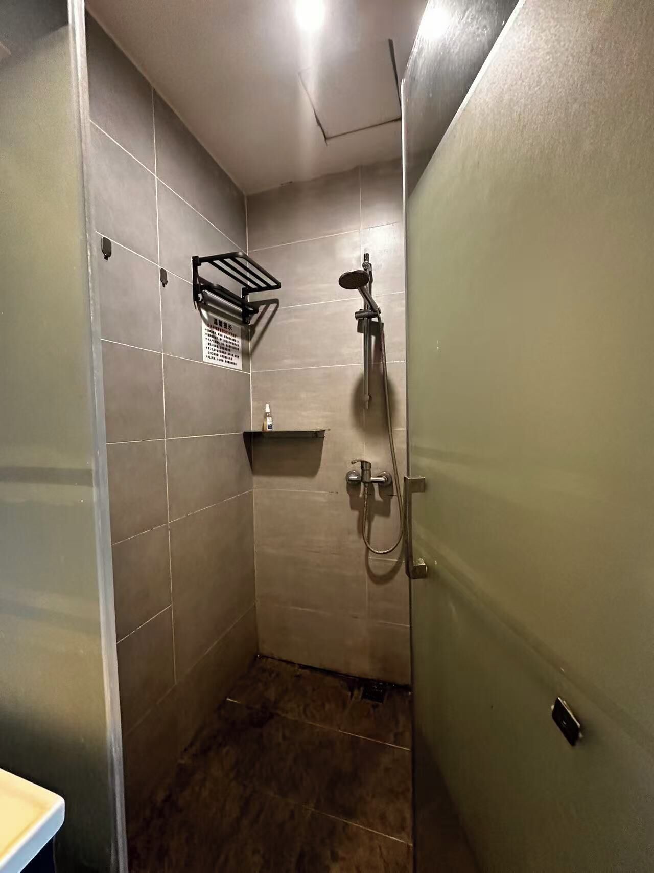 A small, tiled shower room with a showerhead, a handheld shower attachment, and a wall-mounted towel rack.