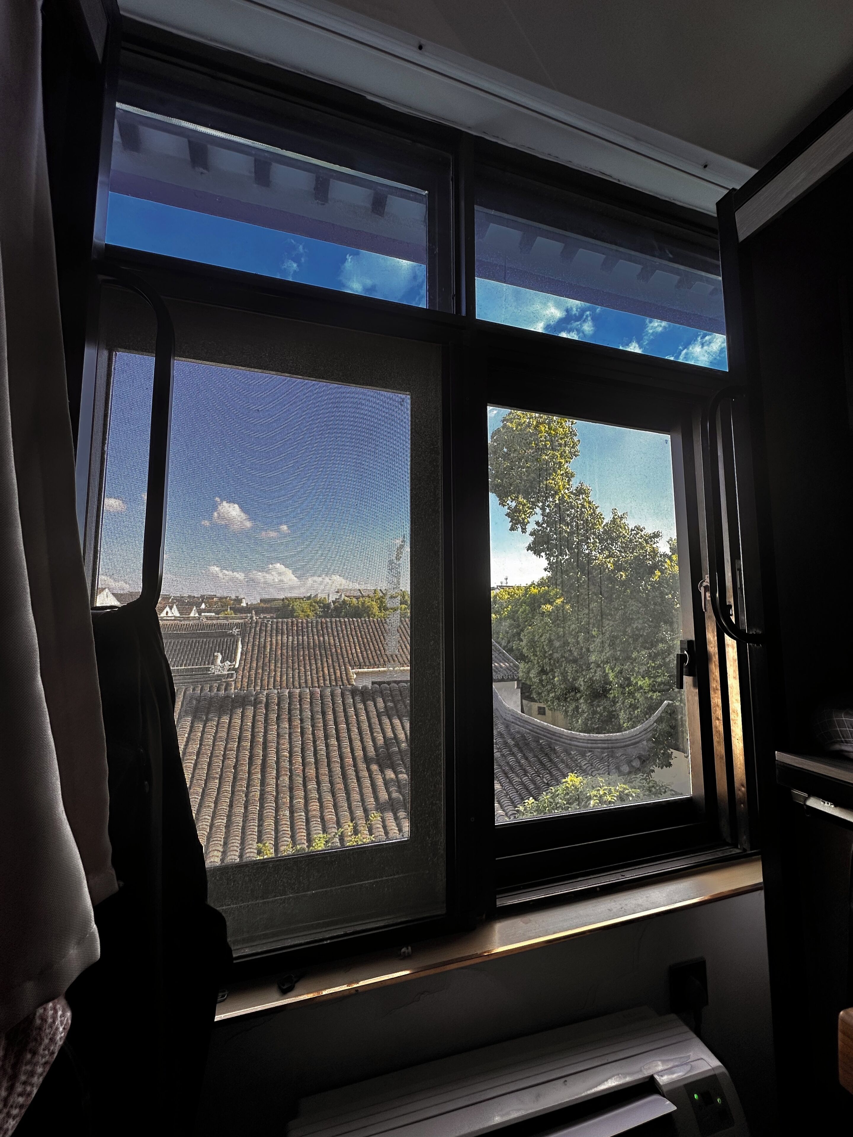 A room with a large window overlooking a traditional tiled roof and trees.