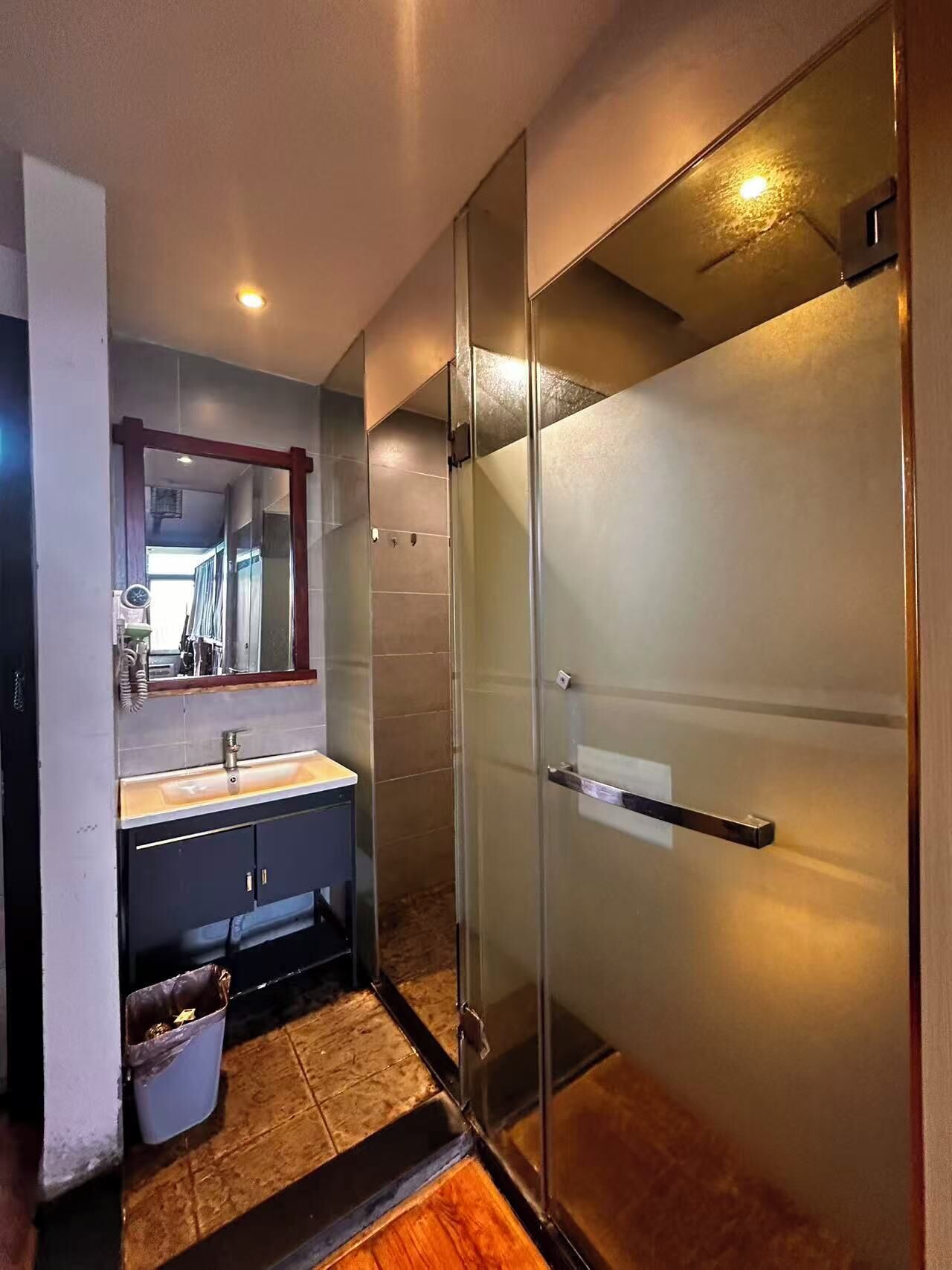 Une salle de bain moderne avec une douche à parois de verre, un lavabo avec un miroir et une poubelle.