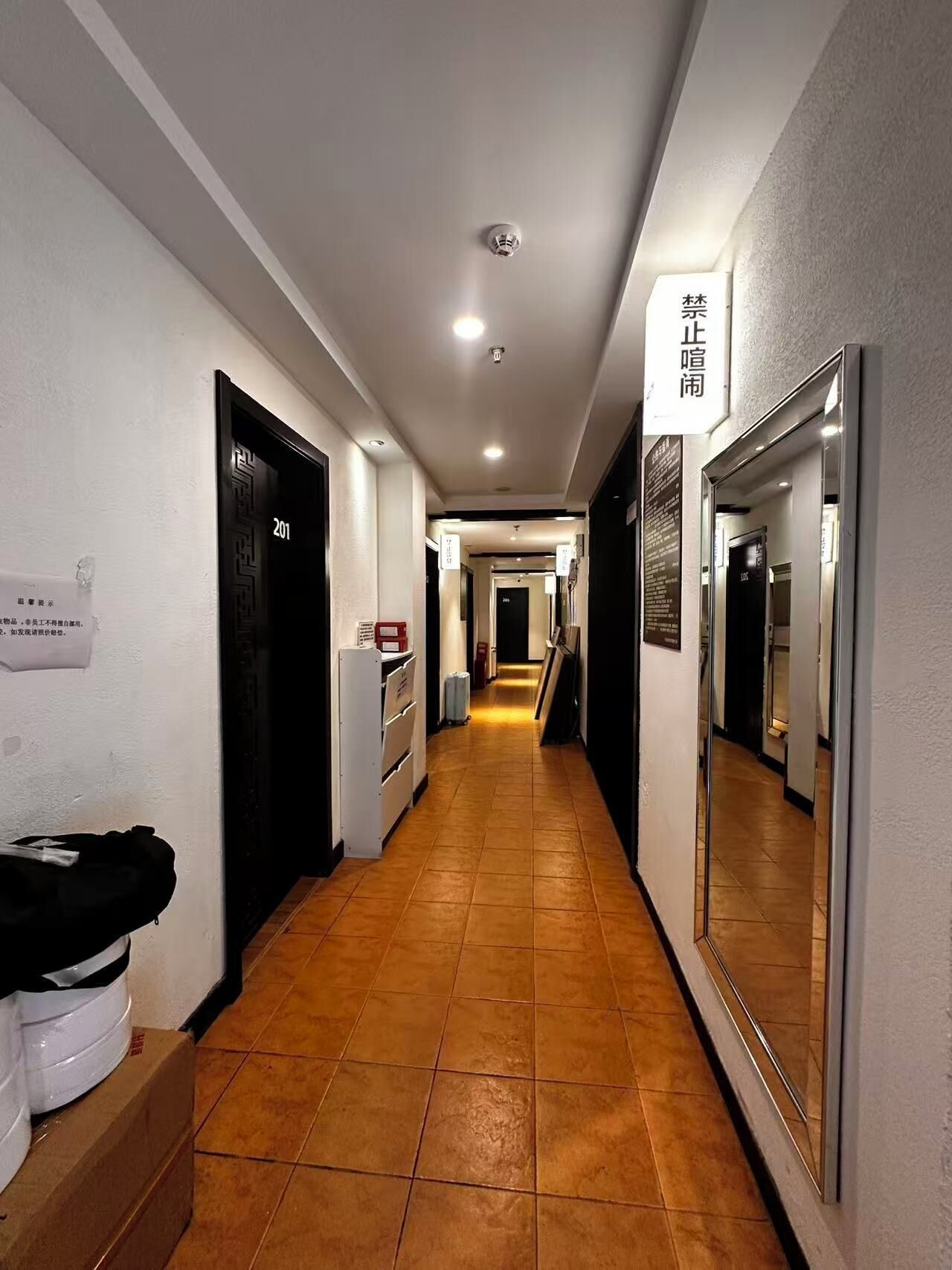 A hotel corridor with a tiled floor, doors, and a mirror on the right wall.