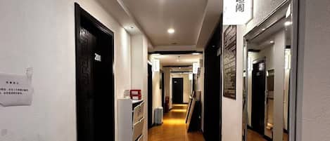 A hotel corridor with a tiled floor, doors, and a mirror on the right wall.