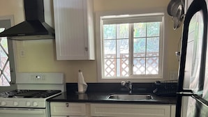Una cocina con armarios blancos, estufa, fregadero y ventana con vista a la vegetación.