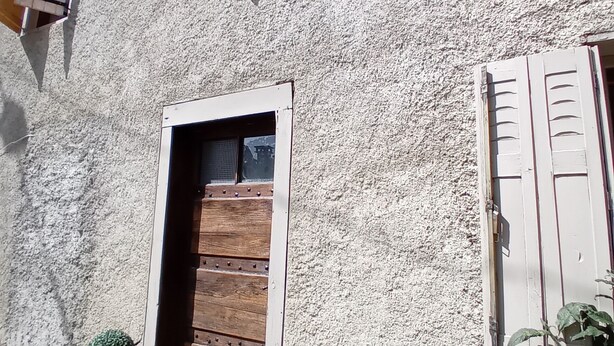 A rustic building with a wooden door, two windows with shutters, and potted plants. - Family home in the mountains! (Portet-d'Aspet)