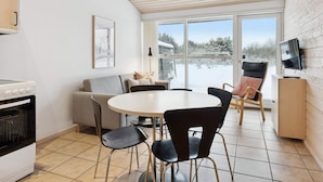 A modern kitchen with a stove, a dining area with a round table and chairs, a sofa, and a TV mounted on the wall. - 4 Star Holiday Home in Pandrup (Pandrup)