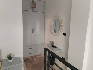 A hallway with a white wardrobe, a small shelf with a decorative item, and a mirror on the wall. - Zahra Sidi-Abdelrahman North Coast (Sidi-Abdelrahman)