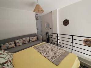 A bedroom with a bed, a sofa, a hanging light fixture, a wardrobe, and a decorative mirror.