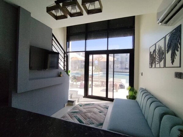 A modern living room with a large window, a flat-screen TV, and a sofa.
