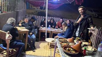 Un área de comedor al aire libre con mesas, sillas y una gran sombrilla roja que da sombra.