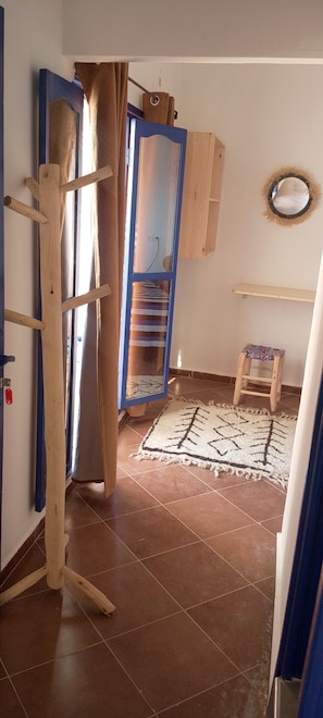 Une pièce avec une échelle en bois, une armoire bleue, un petit tabouret et un tapis à motifs posé sur un sol carrelé.