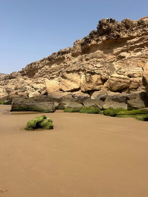A sandy beach with large rocks and a cliff.